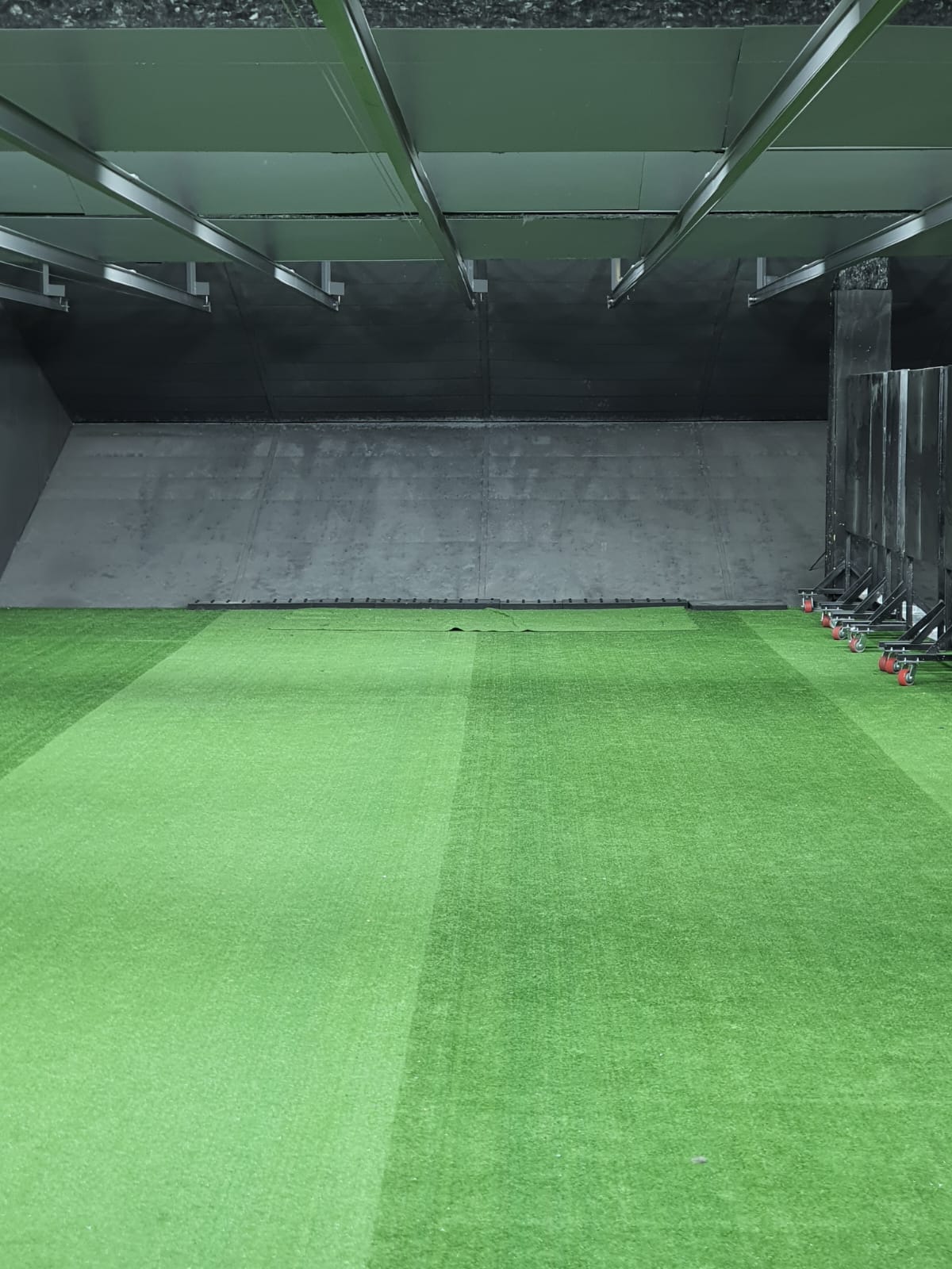 Indoor range bay looking downrange over green turf to the steel backstop