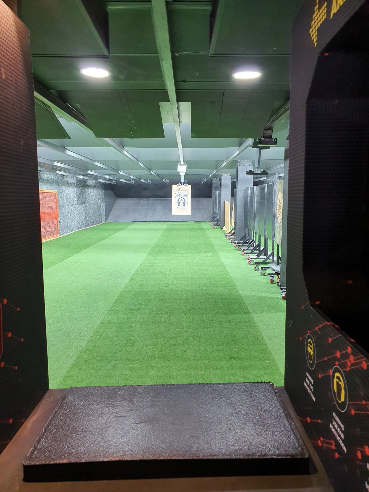 View down an indoor shooting lane to a paper target hanging downrange
