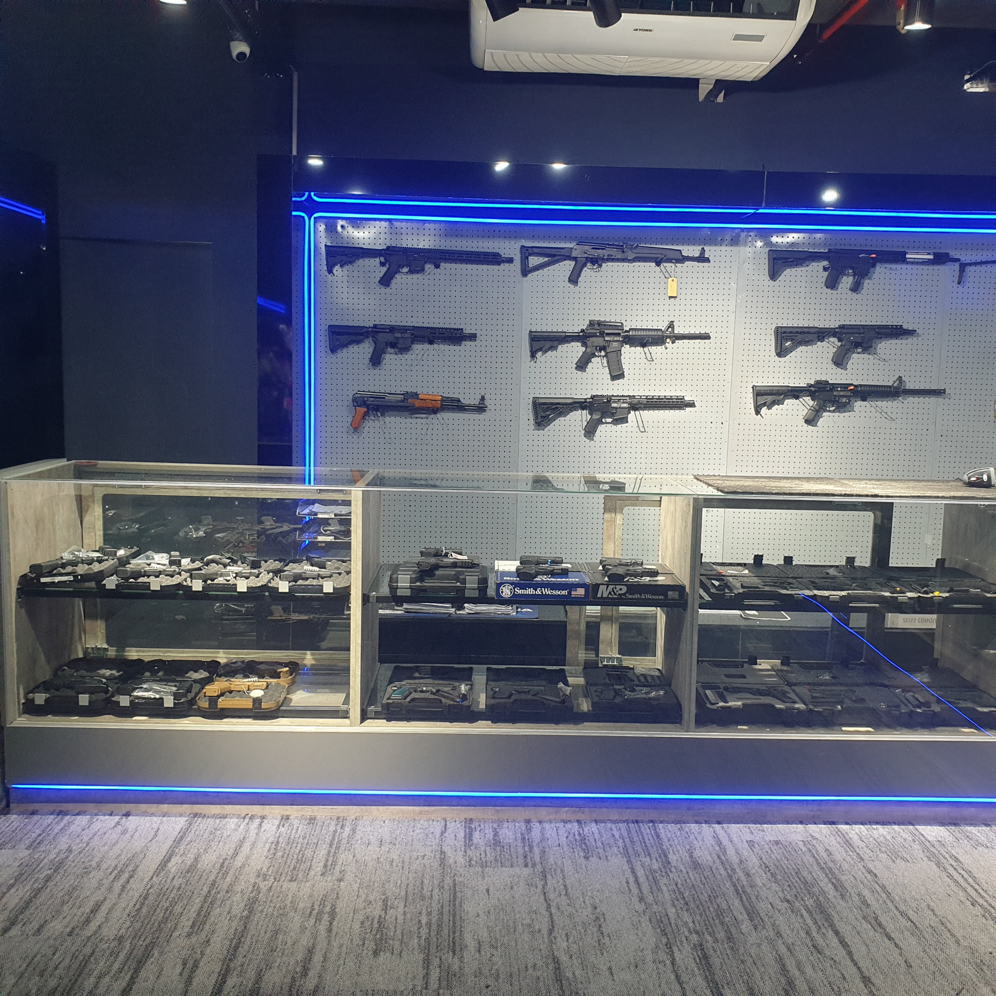 Wide view of the gun shop rifle wall with Smith & Wesson pistol boxes in the display counter