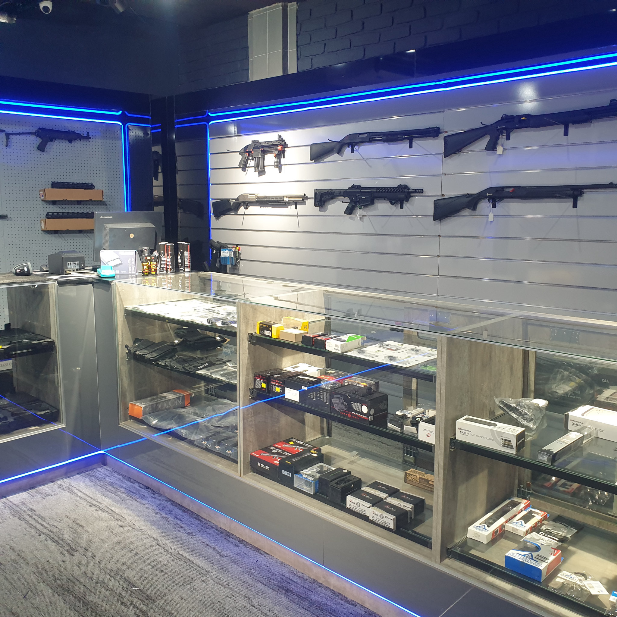 Slatwall shotgun display above glass counters stocked with boxed optics and accessories