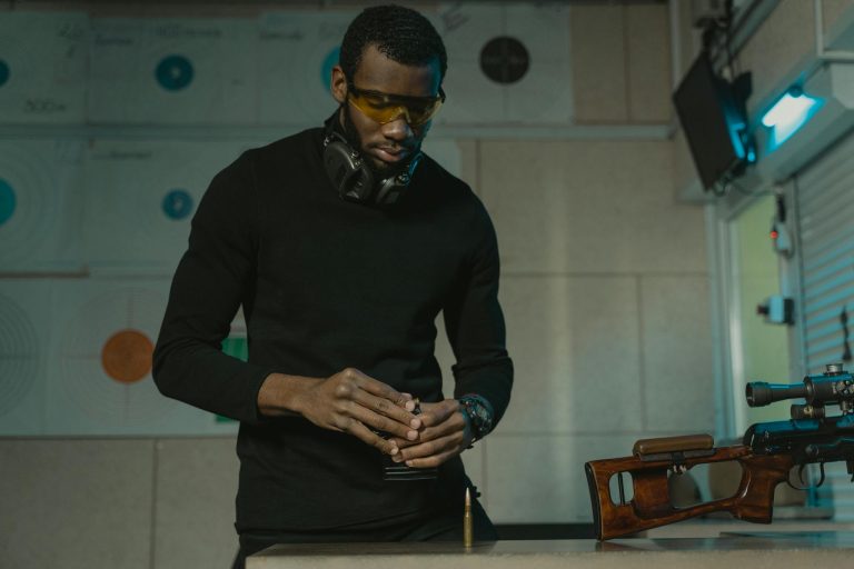 A man wearing safety glasses loads rifle magazines at an indoor shooting range, emphasizing precision and safety.
