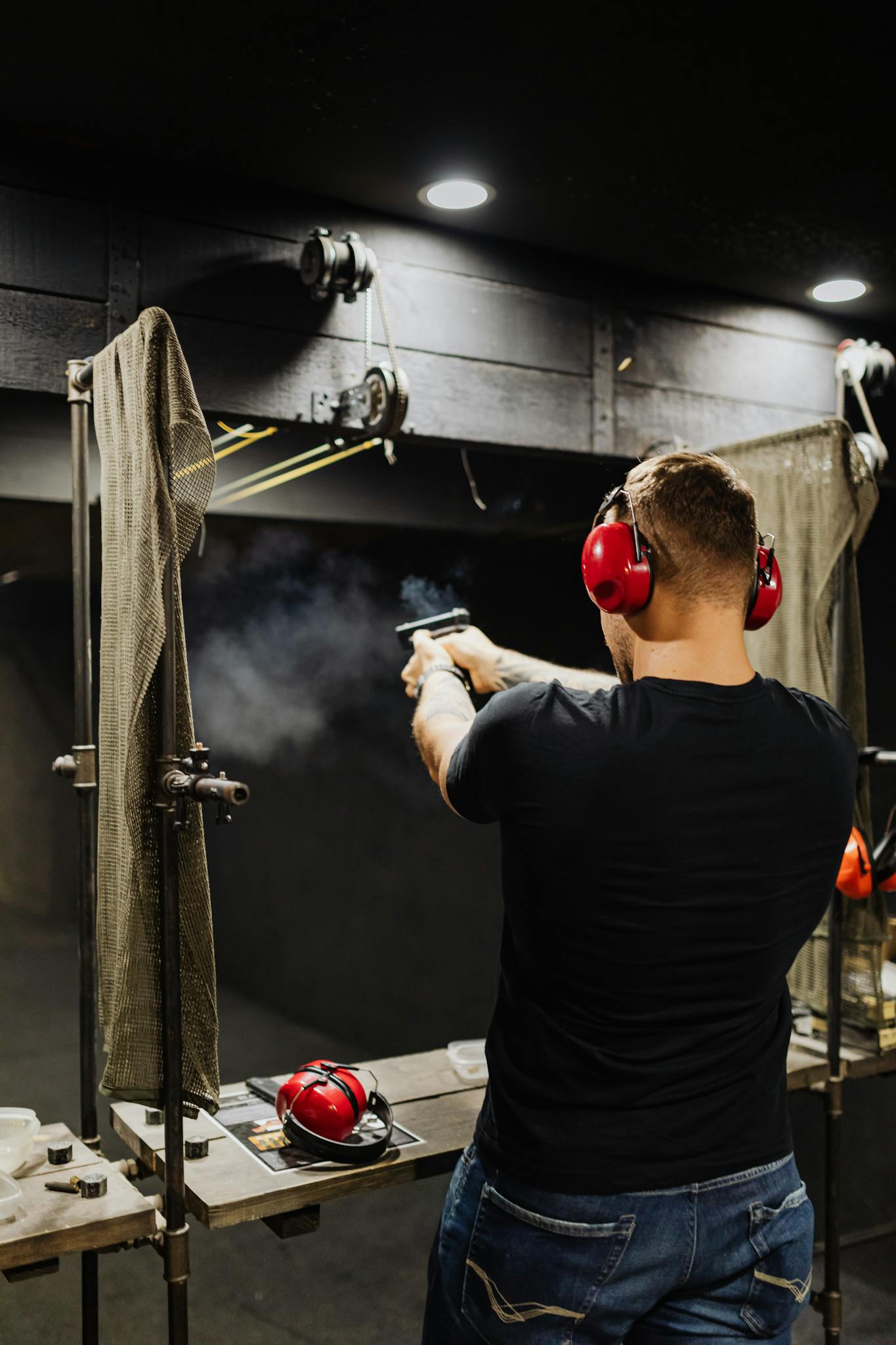 Adult man practicing shooting at an indoor gun range, wearing safety gear and aiming at a target.