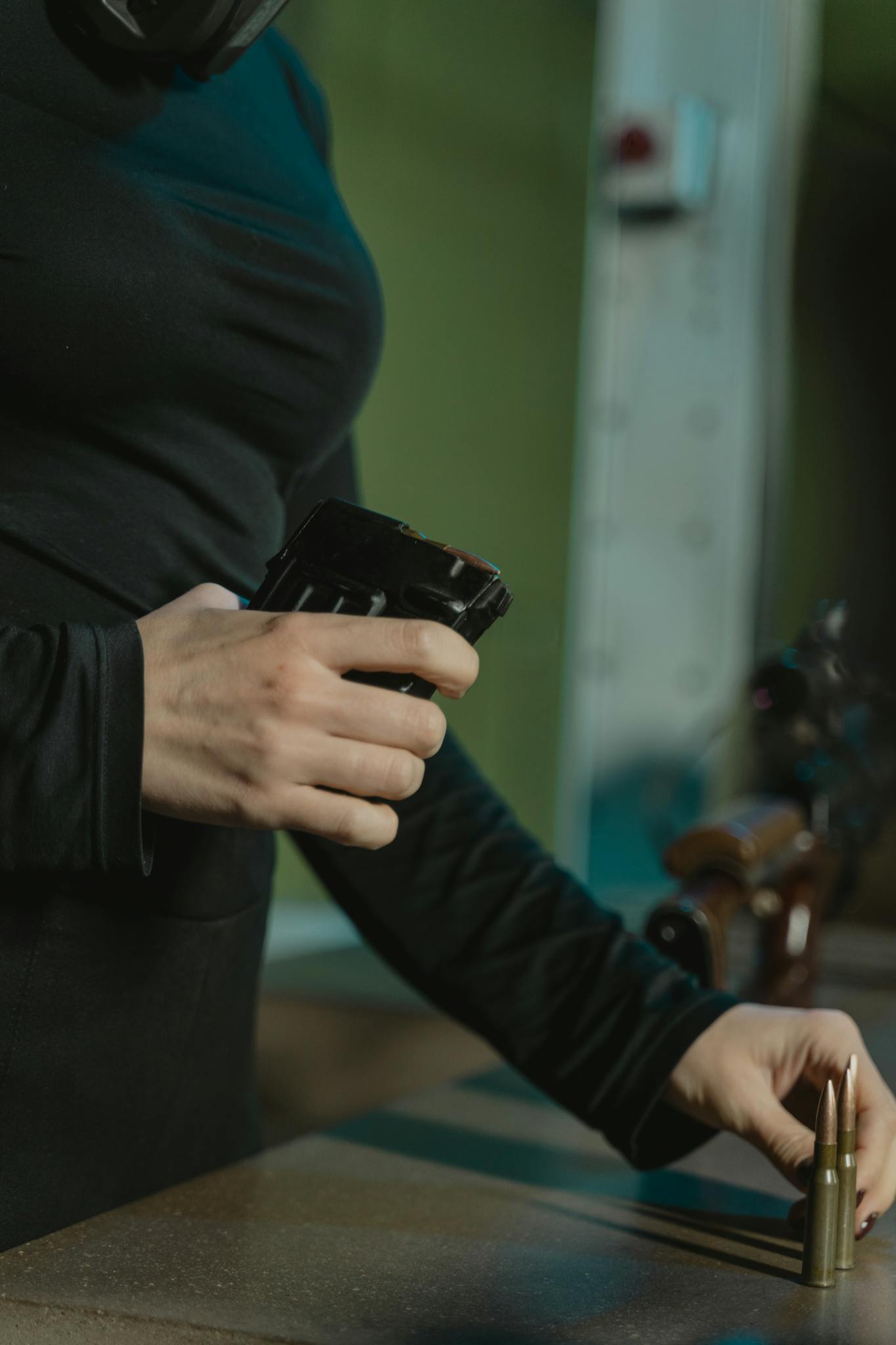 Close-up of a woman in black sleeves loading rifle magazine with bullets indoors.