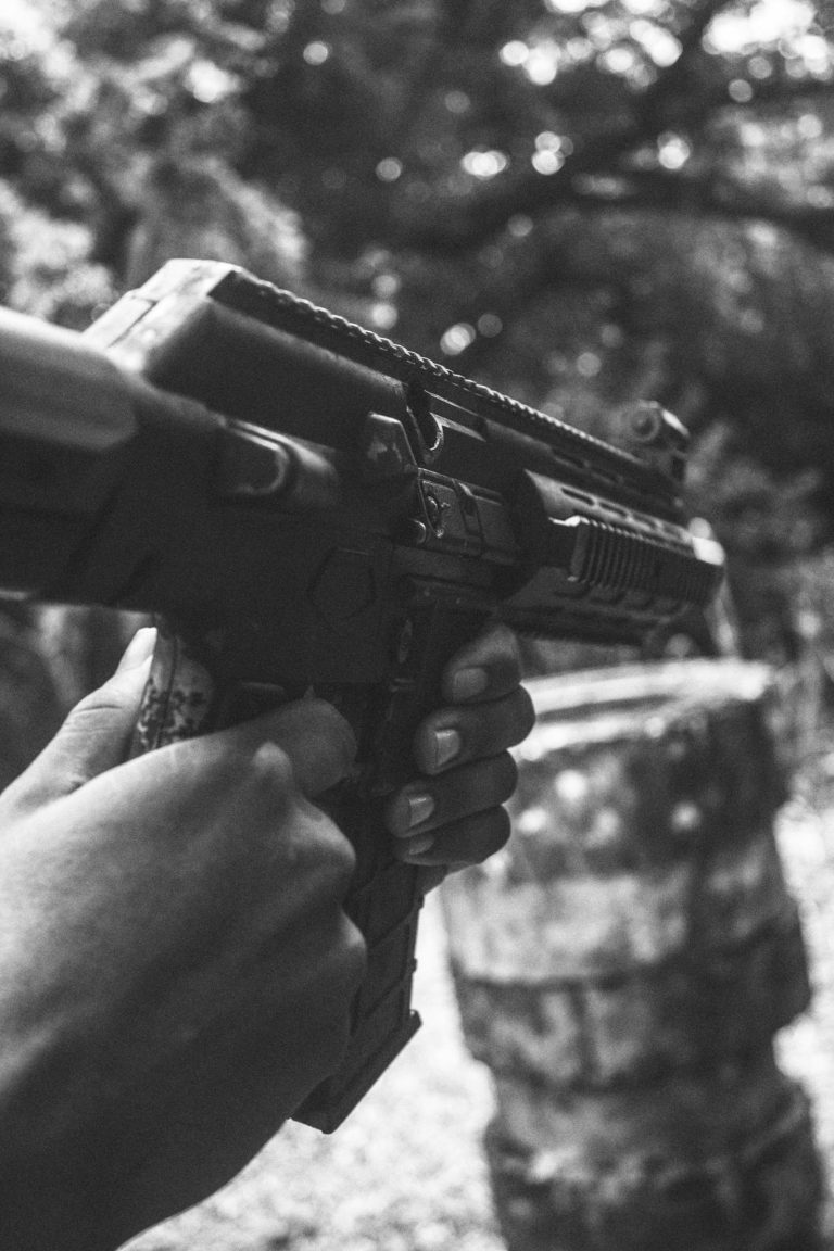 Monochrome image showing hands holding a firearm in an outdoor setting, focused and intense.